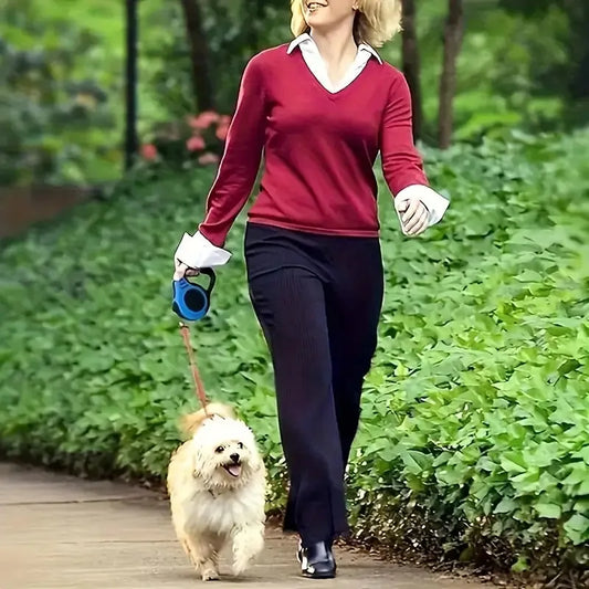 Woman in red sweater walking small fluffy dog on leash along leafy sidewalk in park
