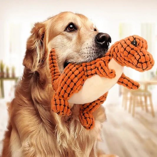 Golden retriever dog indoors holding an orange dinosaur plush toy in its mouth